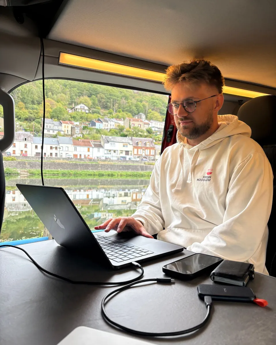 Kobe aan het werk op zijn laptop in een camper aan een rivier